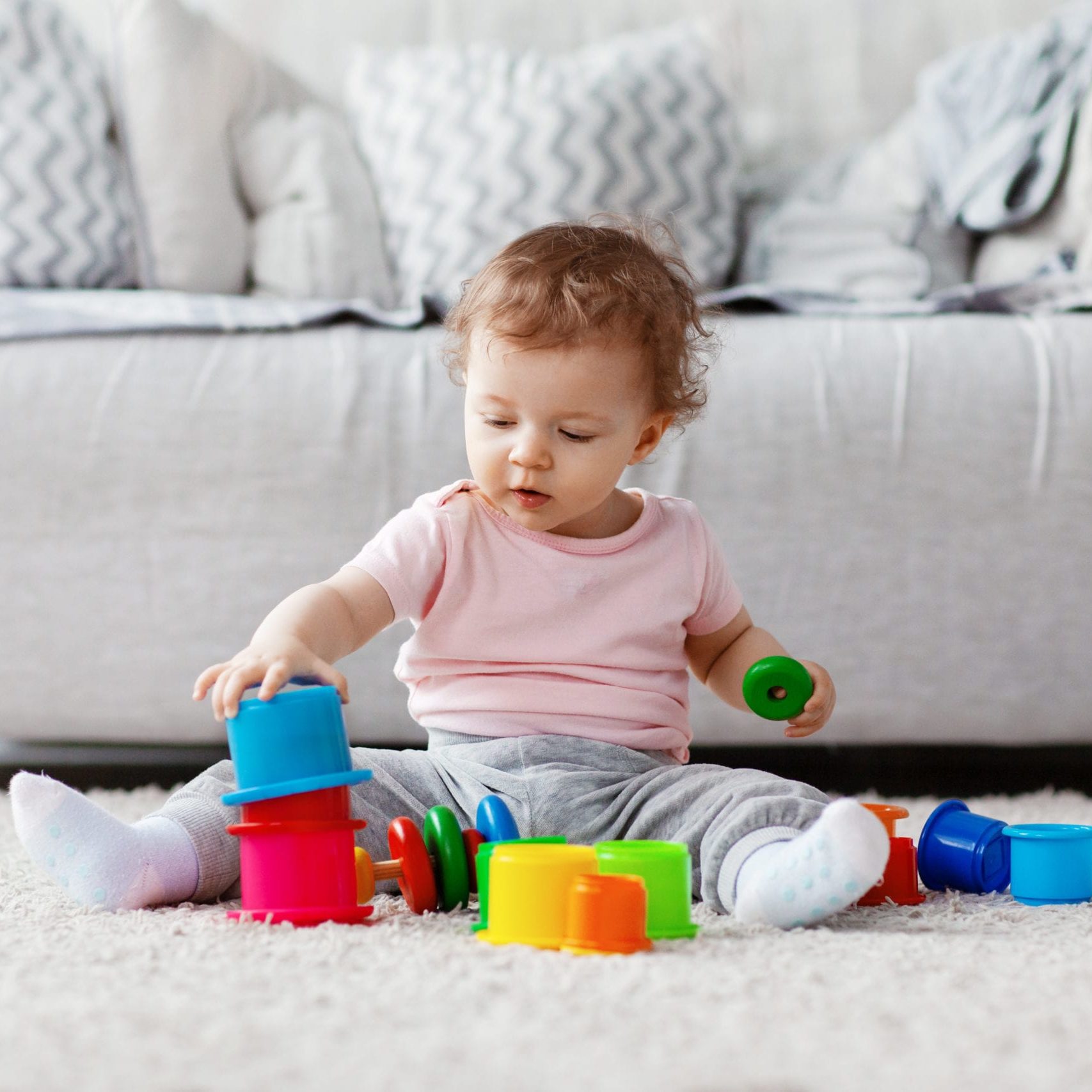 The kid plays on the floor on a light carpet with bright toys, builds a tower. A happy family